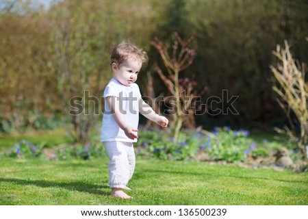 Funny baby girl taking her first steps in the garden