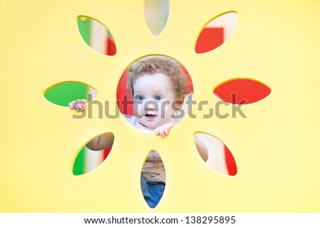 Funny baby girl playing peek-a-boo on a playground