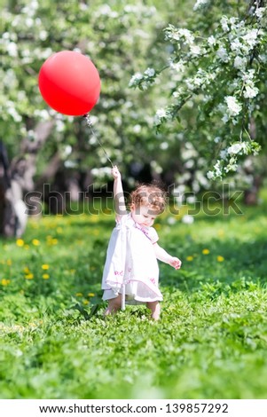 Funny baby girl playing with a red balloon in a garden