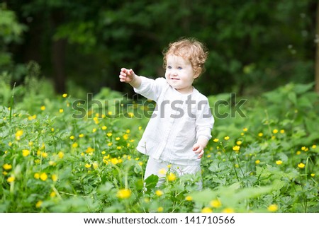 Funny baby girl playing in a field of yellow flowers