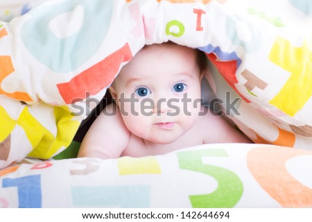 Adorable baby playing peek-a-boo under a colorful blanket