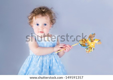 Beautiful little baby girl playing with a wind toy, on light blue background