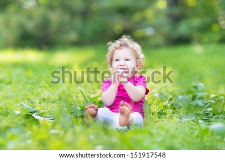 Adorable funny curly baby girl eating candy in a sunny park