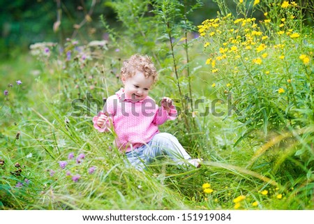 Funny adorable baby girl walking in the garden among beautiful wild flowers