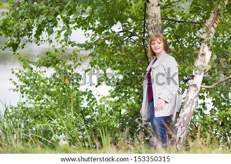 Beautiful lady in an elegant coat relaxing at a lake shore in autumn