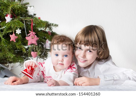 Family portrait of a little boy and his adorable baby sister playing under a red and white decorated Christmas tree