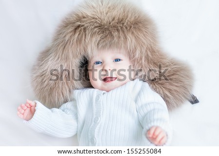 Funny laughing baby girl wearing a huge winter hat and a warm knitted jacket