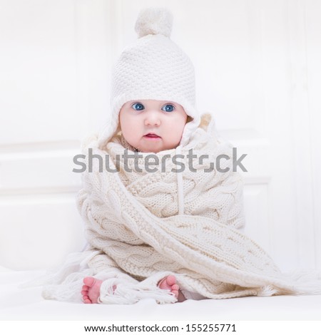 Funny Cute Baby With Big Blue Eyes Wearing A Hat And A Huge Knitted Scarf