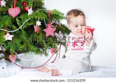 Adorable baby girl playing with a toy bell under a Christmas tree