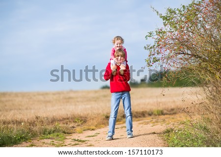 Happy laughing brother and his baby sister playing together in a sunny golden autumn field