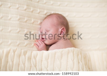 Adorable tiny newborn baby sleeping under a warm knitted blanket