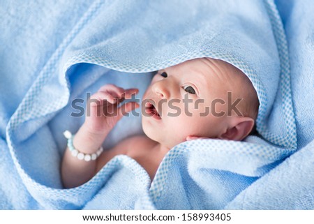 Funny newborn baby in a blue towel after bath