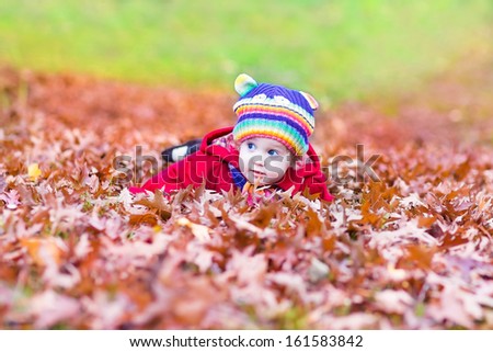 Funny little baby girl playing with colorful red autumn leaves