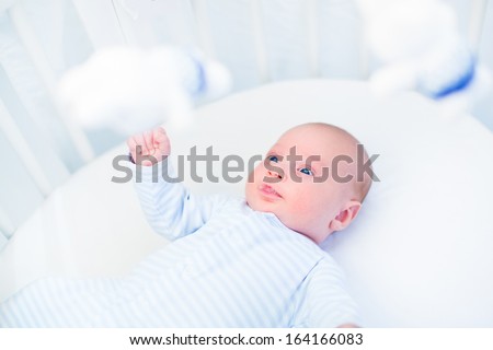 Cute newborn baby boy watching toys in a white round crib