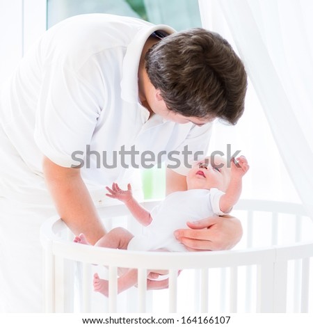 Happy young father putting his newborn baby in a white crib with canopy