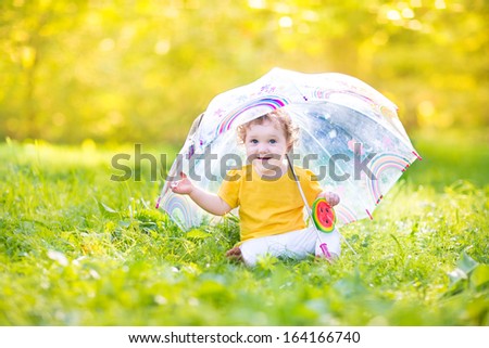 Cute funny baby girl playing in the rain under a colorful umbrella
