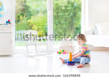 Cute Toddler Girl Playing With A Pyramid Toy In A White Room With A Big Window With Garden View