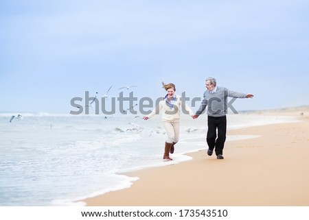 Happy mature couple running at a beautiful winter beach with seagulls