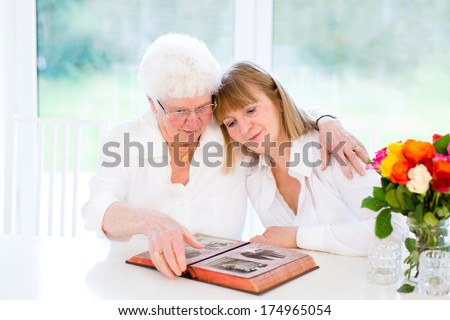 Beautiful woman and her loving mother watching together a black and white photo album in a white sunny living room
