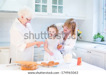 Funny toddler girl baking an apple pie with her grandmothers in a sunny white kitchen