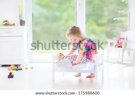 Cute Curly Toddler Girl Playing With Her Bear In A Sunny Room With Big Garden View Windows