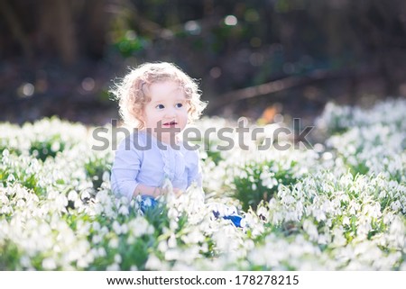 Adorable curly toddler girl playing with first spring flowers in a beautiful spring sunny park
