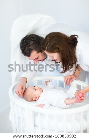 Happy young parents looking at their cute smiling baby son in a white round crib