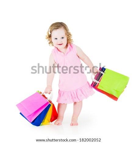Adorable little girl with curly hair wearing a pink dress is happy after sale and special offer shopping showing her colorful bags