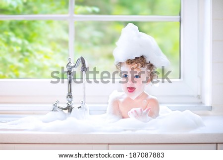 Cute happy baby girl with big blue eyes playing with water in a