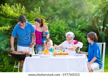 Happy big family - young mother and father with kids, teen age son, cute toddler daughter and a little baby, enjoying BBQ lunch with grandmother eating grilled meat in the garden with salad and bread
