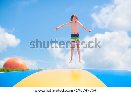 Happy laughing boy jumping on a colorful trampoline having fun at a party in a recreation park during summer vacation