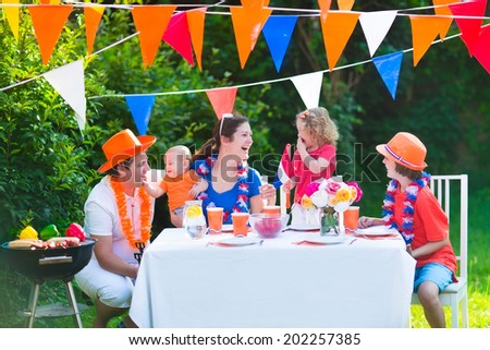 Happy big Dutch family with kids celebrating a national holiday or sport victory having fun at a grill party in a garden decorated with flags of Netherlands, screaming Hup Holland