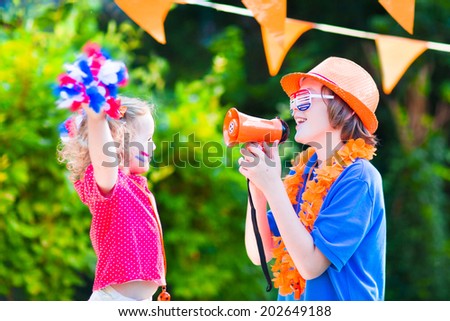 Two Dutch children, teenager boy and funny little girl, fans and supporters of Dutch football team, celebration championship victory playing with whistles decorated with flags