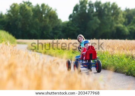 Two happy children, laughing boy and his funny little sister, adorable toddler girl, playing together enjoying a go cart car ride on a country road in a beautiful autumn field
