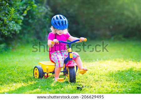 Cute funny toddler girl riding her bike wearing a safety helmet enjoying a nice sunny day in a summer garden playing outdoors
