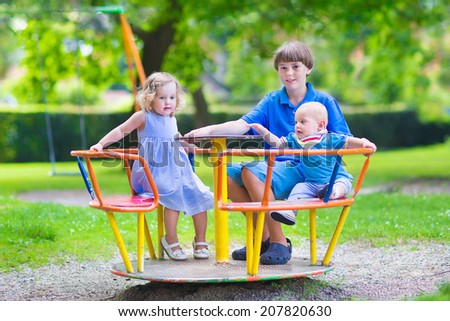Three happy children, laughing teenager boy, cute baby and adorable toddler girl, brothers and sister playing together on a playground swing enjoying a sunny hot summer day
