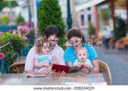 Happy family of four, young parents and their two kids, adorable toddler girl and cute baby boy enjoying lunch at a beautiful outside cafe in a small traditional German town