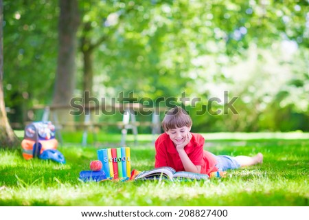 Happy laughing teenager student boy relaxing on a green lawn in the school garden reading books and having healthy snack, back to school concept