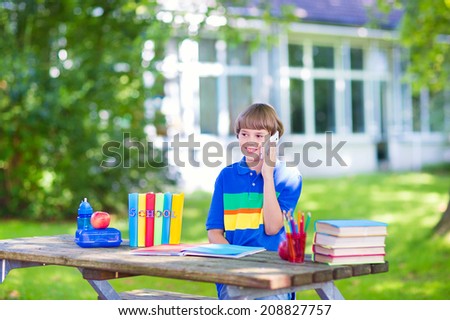 Happy laughing teenager student boy in the school yard talking on his mobile phone, reading books and having healthy snack, back to school concept