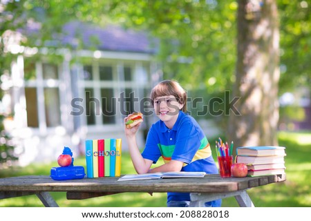 Happy laughing teenager student boy in the school garden reading books and having healthy snack, back to school concept