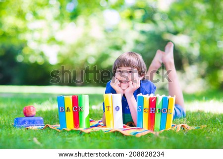 Happy laughing teenager student boy in the school garden relaxing on a lawn reading books and having healthy snack, back to school concept