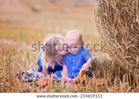Two children, funny toddler girl and a little baby boy, playing in a field with hay rolls eating pretzels during Oktoberfest in Germany. Sister kissing and hugging her little brother