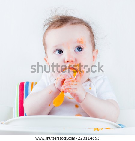 Sweet messy baby eating a carrot in a white high chair