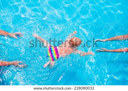Cute little baby swimming underwater from mother to father in a pool, learning to swim lessons and early development concept