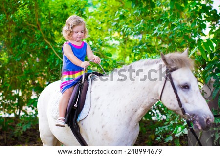 Cute little toddler girl having fun on a horse ride enjoying family trip to a zoo on a hot summer day