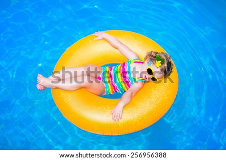 Cute funny little toddler girl in a colorful swimming suit and sun glasses relaxing on an inflatable toy ring floating in a pool having fun during summer vacation in a tropical resort