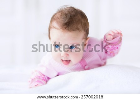 Cute funny baby girl in a pink cardigan having fun learning to crawl