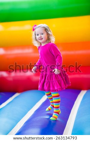 Cute funny preschool little girl in a colorful dress playing, jumping and bouncing in an inflatable castle having fun at a children birthday party on a kids playground in summer