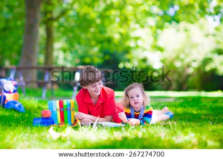 Children in school yard. Happy laughing teenager student boy and preschool girl in the school garden reading books and having apple for healthy snack, back to school concept