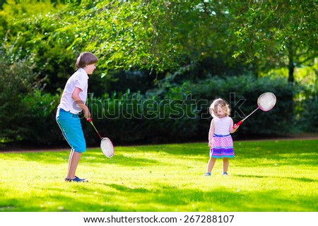 Active children playing badminton. Two happy kids, boy and girl having fun on a family picnic in a park, enjoying sport games, running and jumping with tennis racket on a hot summer day outdoors.